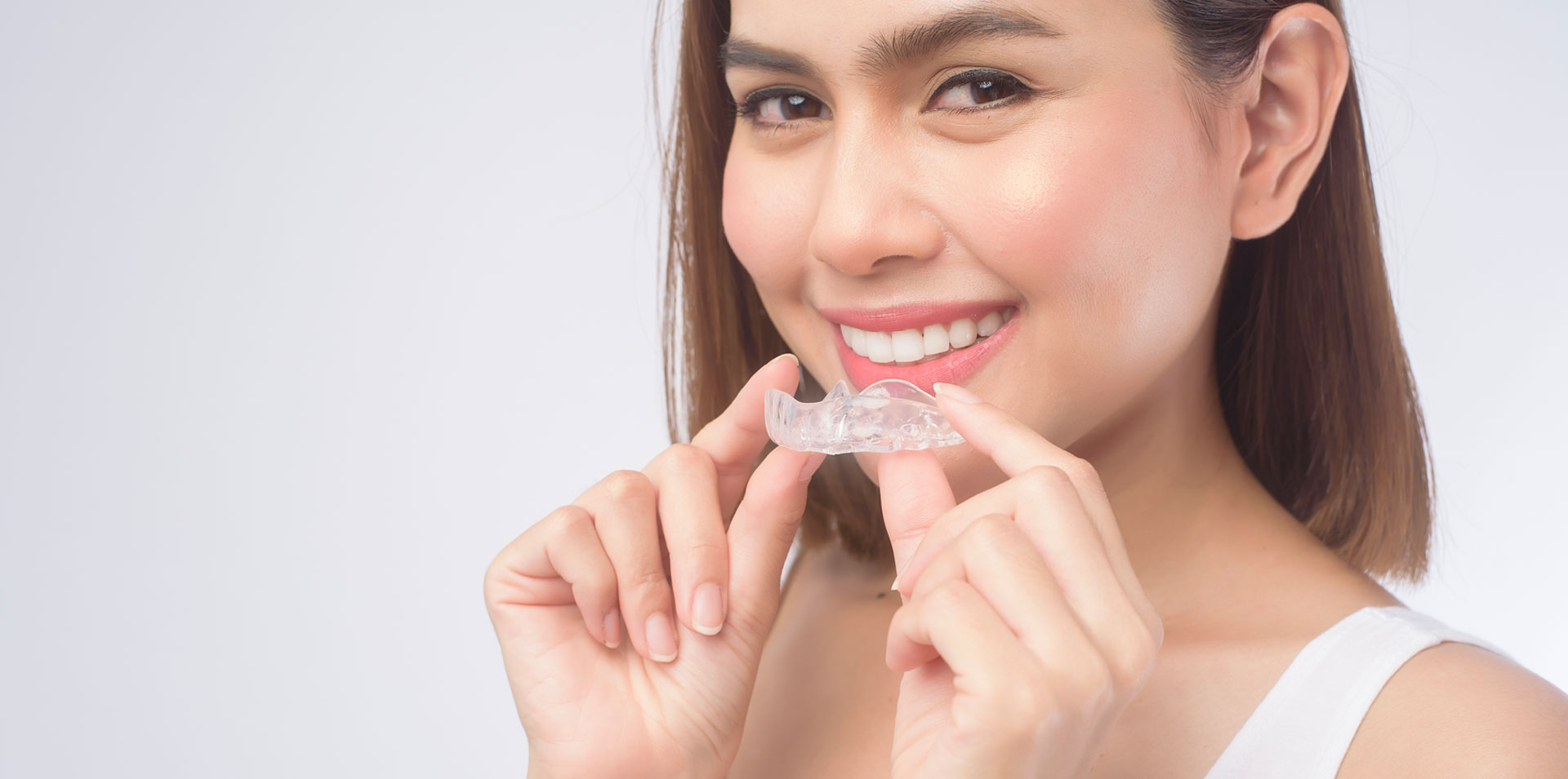 A young smiling woman holding invisalign braces